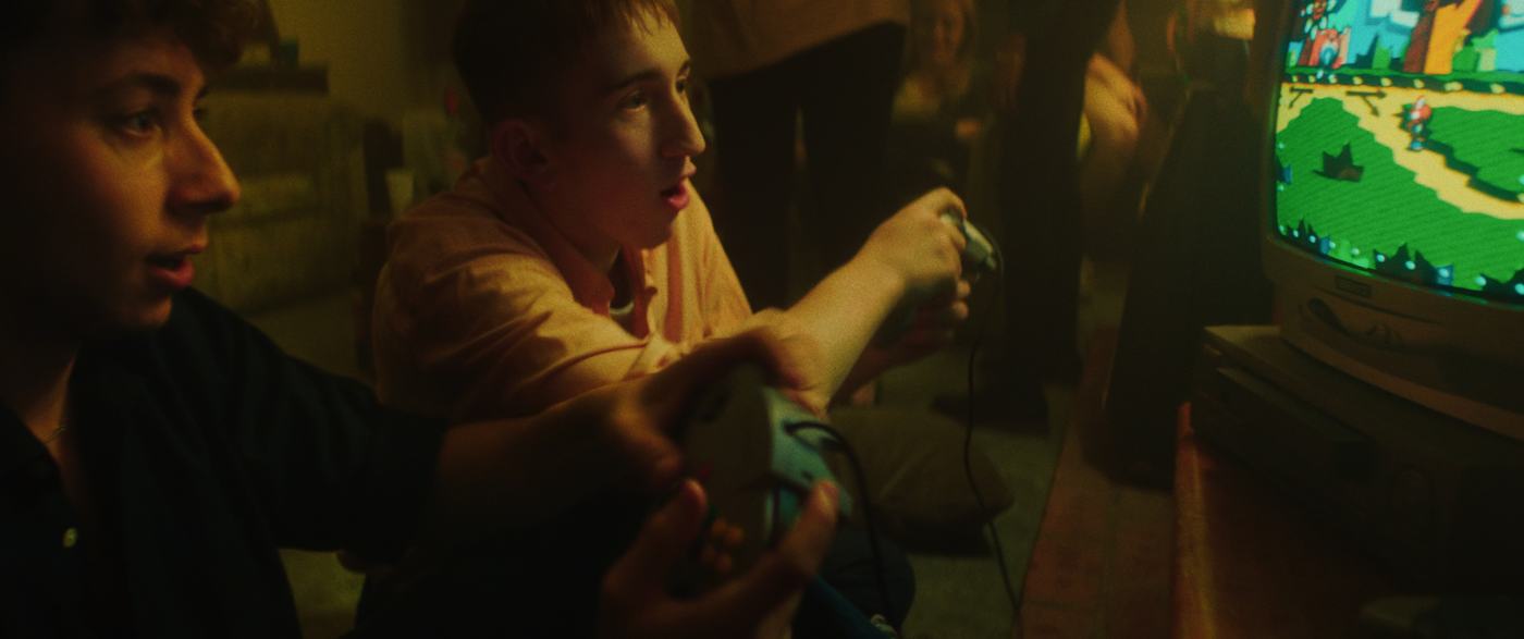 Two teenagers playing a console game in front of a CRT, warm lamplight